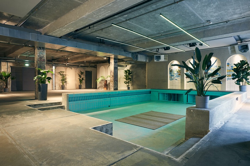 leerer türkisfarbener Pool in einem Raum mit viel Sichtbeton und Pflanzen